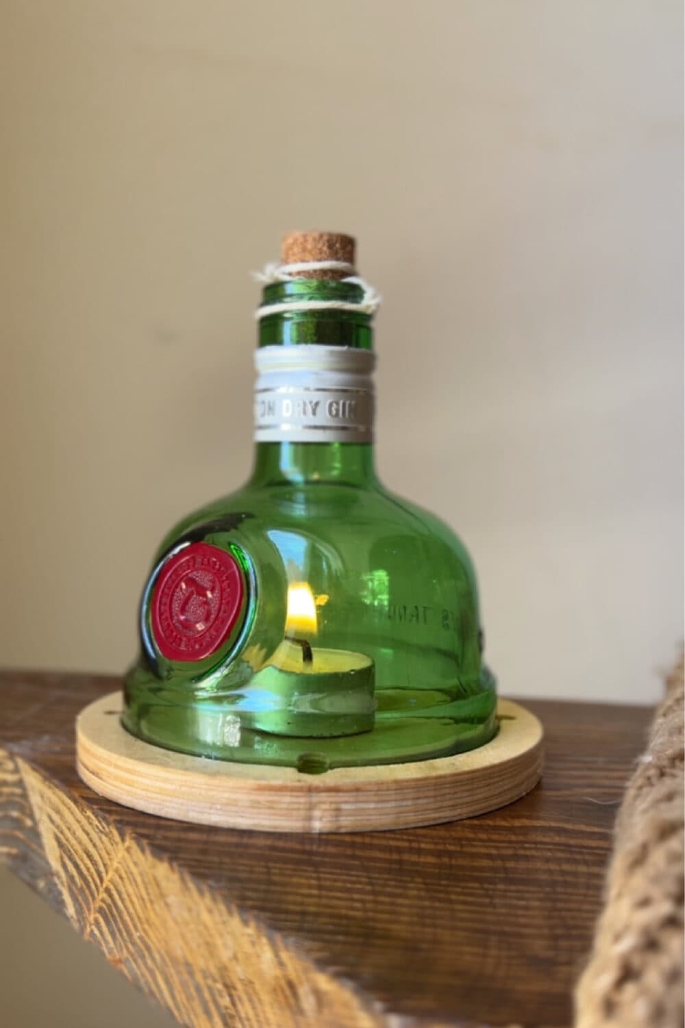 The top of a green glass bottle with a cork and twine, set over a tealight on a round wooden base, on a wooden shelf